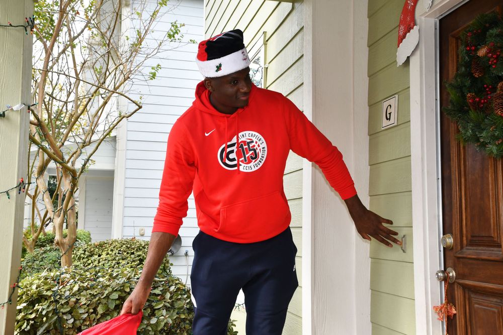 Person in red hoodie with sports logo and Santa hat standing on front porch.