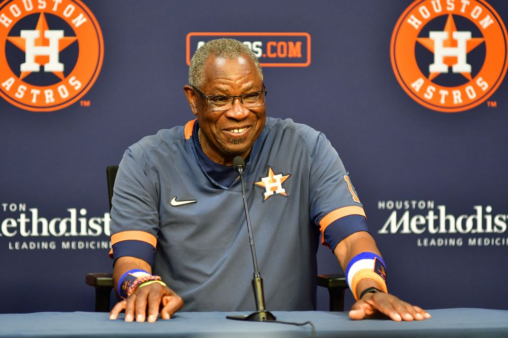 Houston Astros manager smiles during press conference with team logos in background.