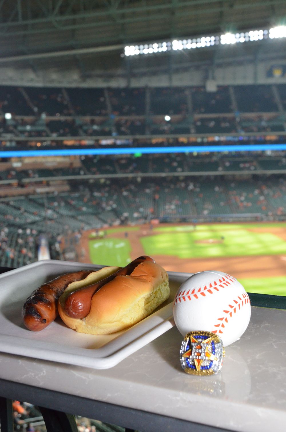 Baseball stadium view with hot dog and baseball on ledge during game.