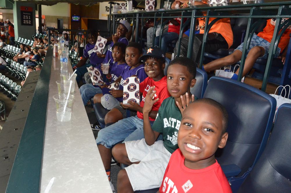 Young sports fans smile excitedly while seated in stadium seats at a baseball game.
