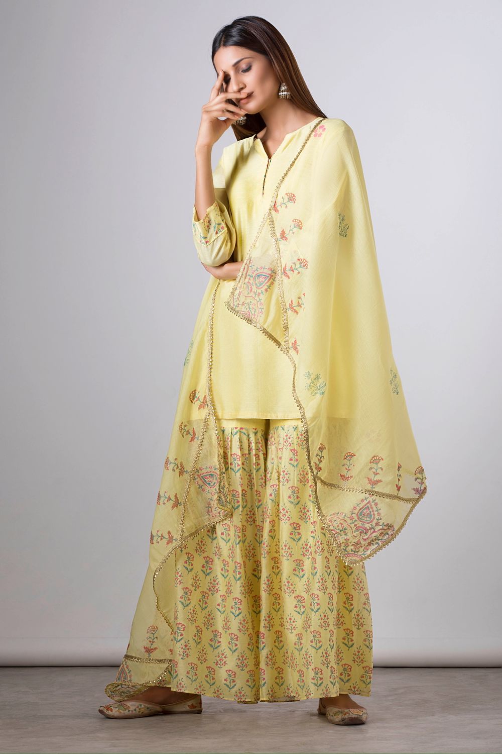 Woman in yellow floral embroidered kurta set with sharara pants and dupatta, traditional Indian ethnic wear.