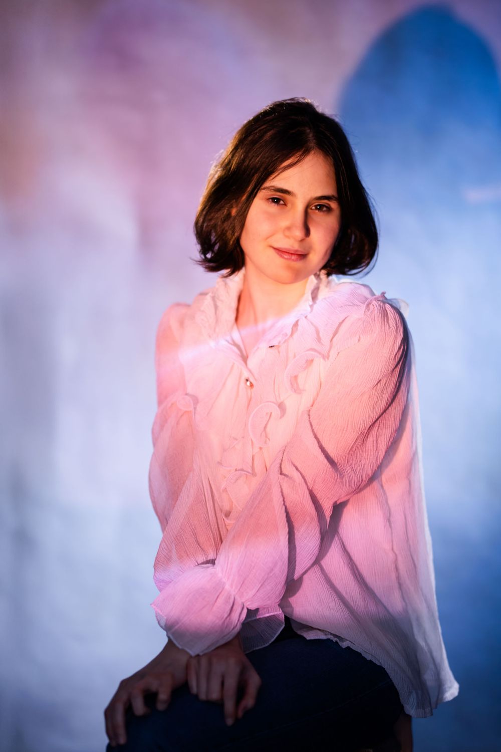 Portrait of someone in a pink blouse against a dreamy blue and purple gradient background.