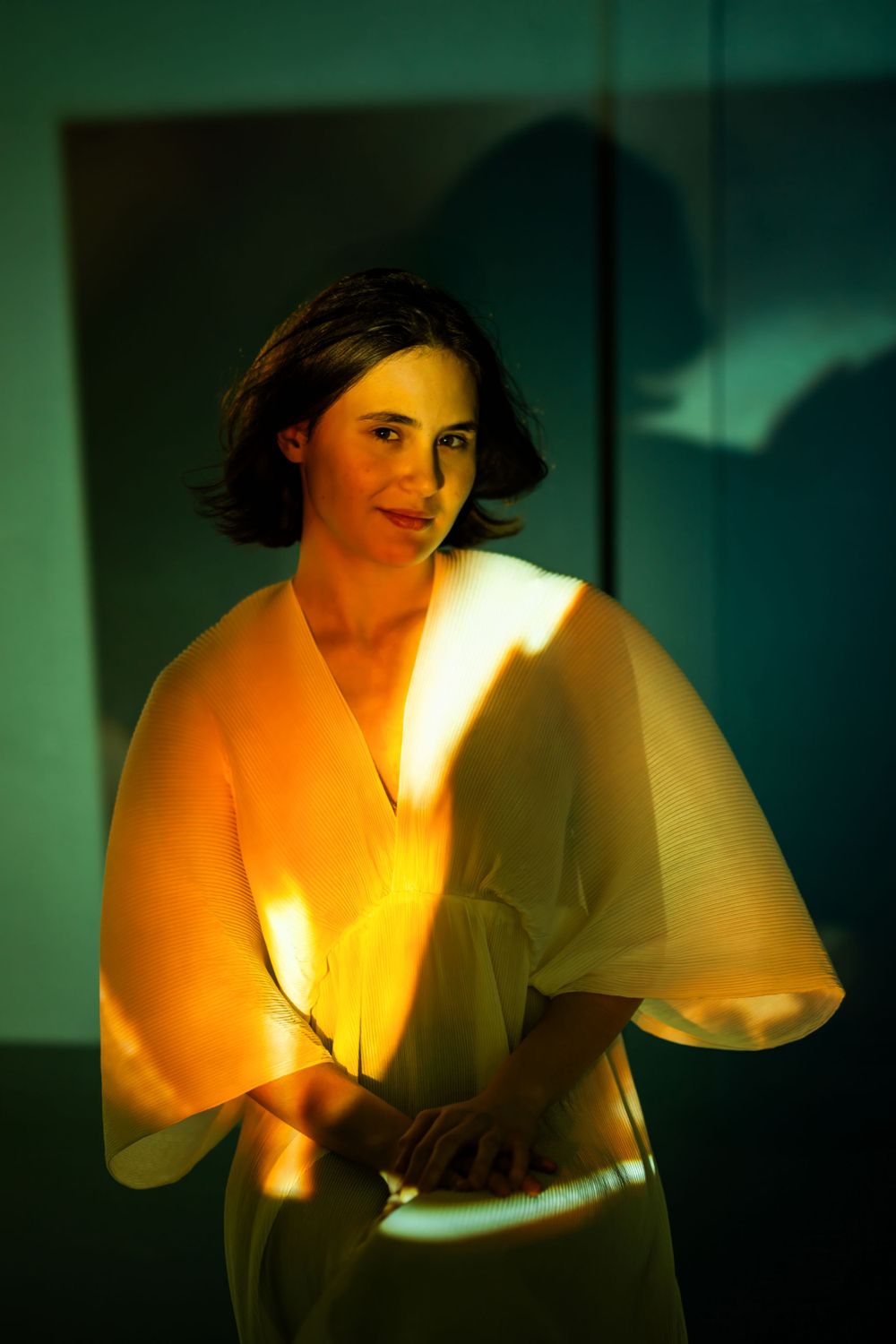 Portrait with dramatic orange and green lighting highlights a person in a flowing white blouse with soft shadows.