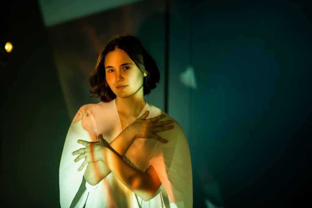 A dramatic portrait shot in moody lighting with green and blue tones showing a figure wrapped in white fabric.