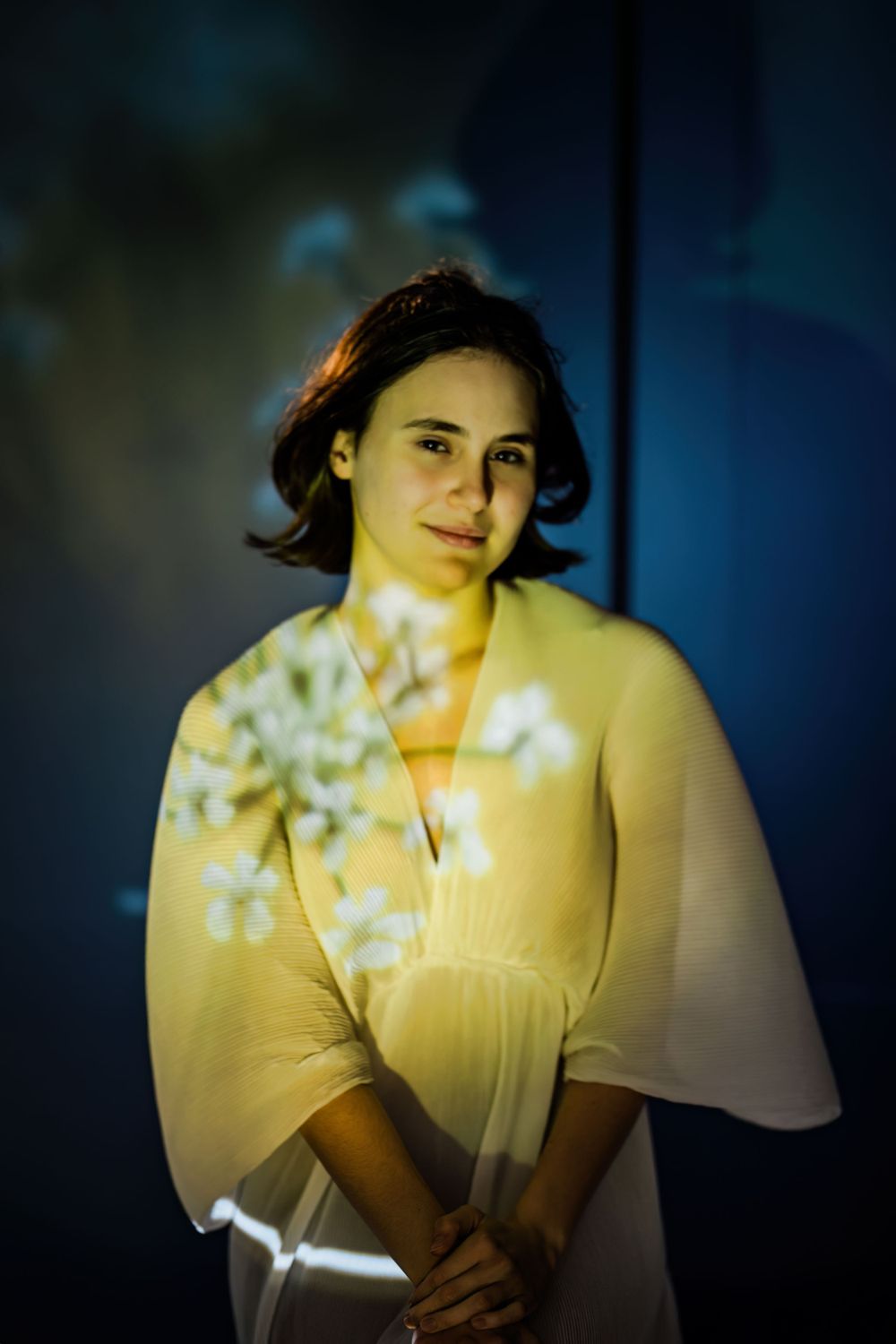 Portrait in yellow dress photographed against dark background with ethereal light and floral shadows creating dreamy ambiance.