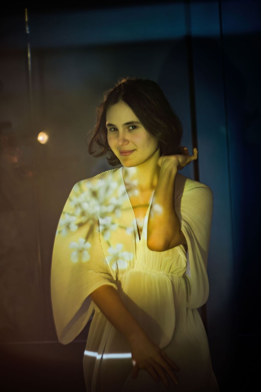 Artistic portrait of someone wearing a white dress in moody lighting with atmospheric light patterns projected on the wall.