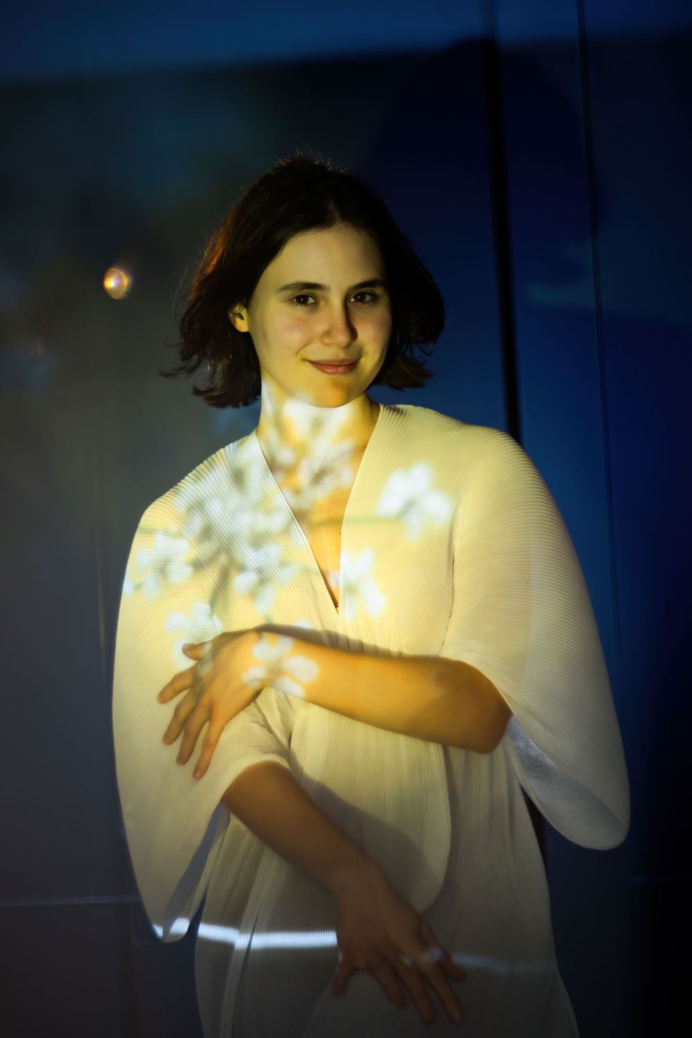 Artistic portrait in soft lighting features someone wearing a flowing white outfit against a dark blue background.