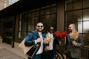 Wedding party members walk together along a cobblestone path between brick buildings.