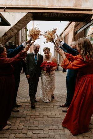 Wedding party members in red dresses and formal attire create a celebratory walkway outdoors.