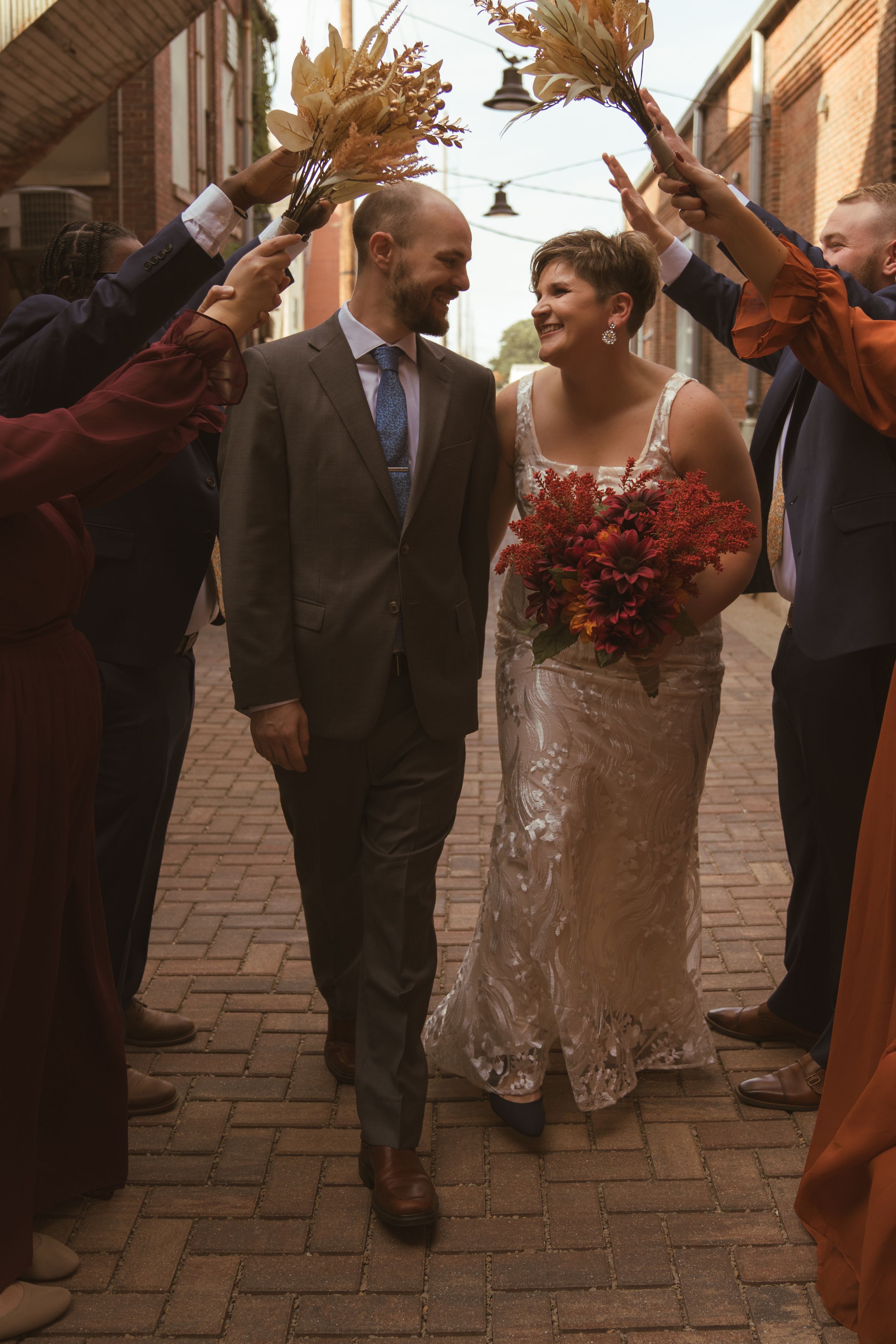 Wedding couple and guests dancing joyfully on a brick paved street during golden hour.