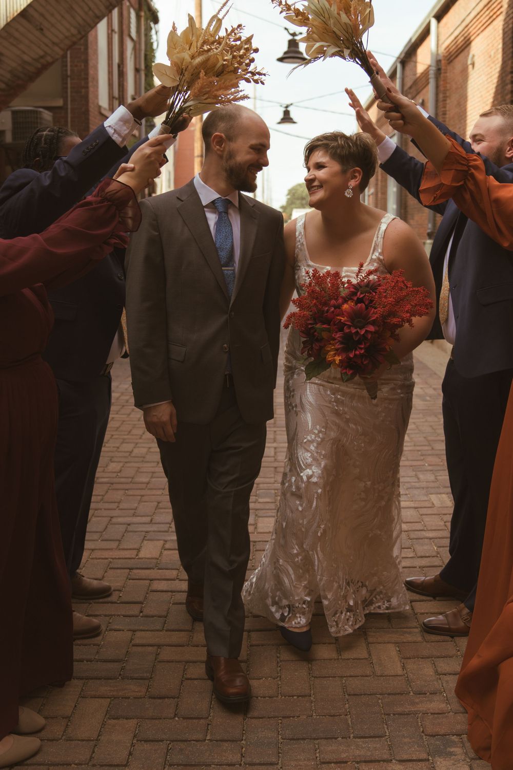 Wedding couple and guests dancing joyfully on a brick paved street during golden hour.