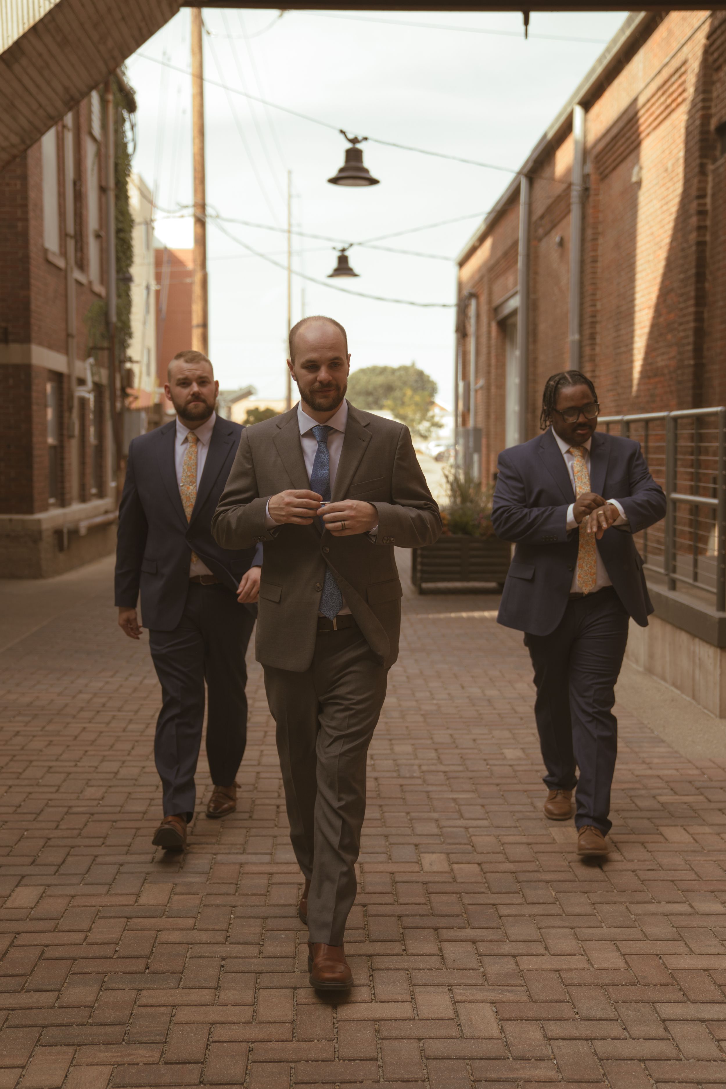 Groomsmen in suits walking confidently down a brick-lined street.