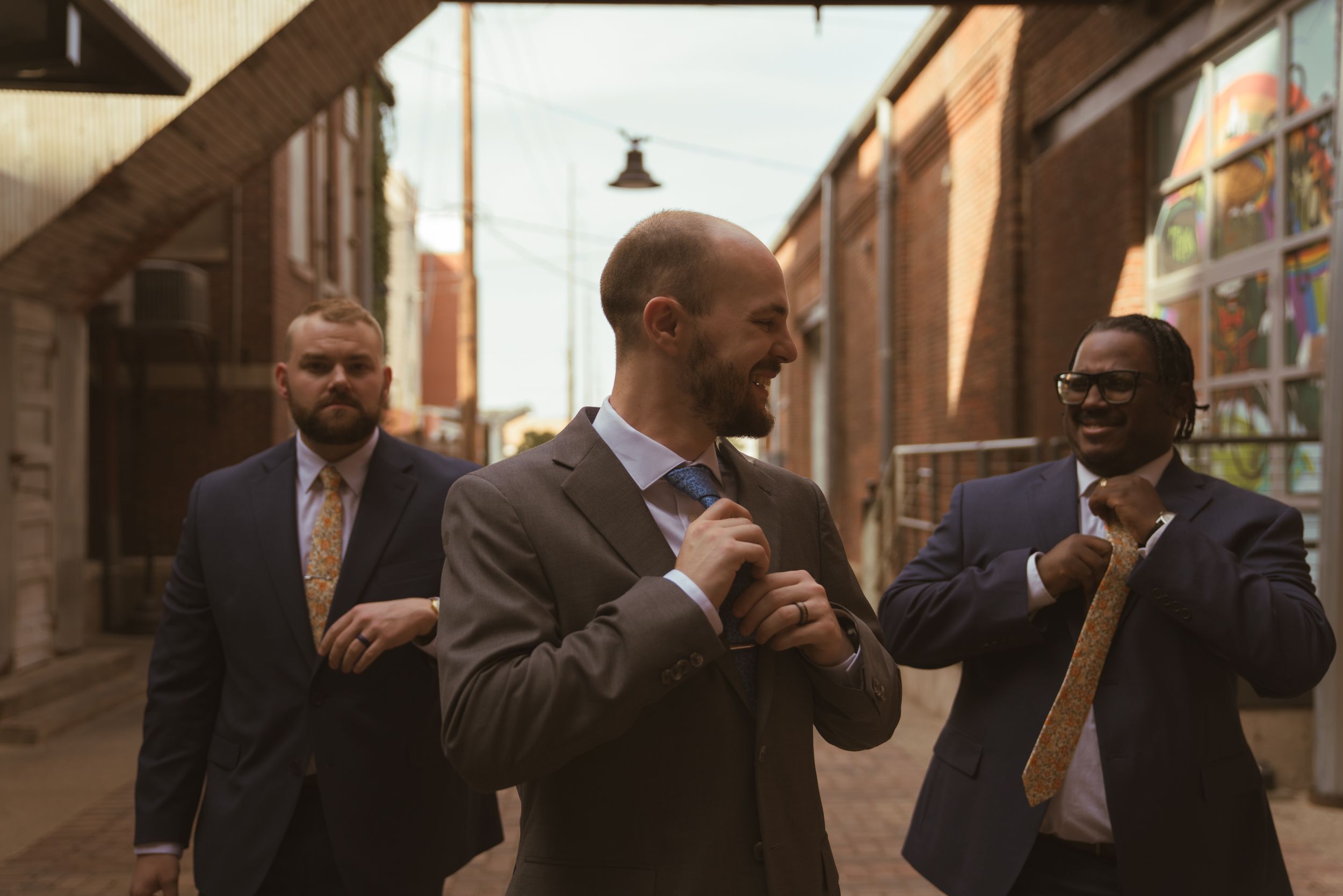 Wedding party members walking and smiling along an industrial brick building corridor.