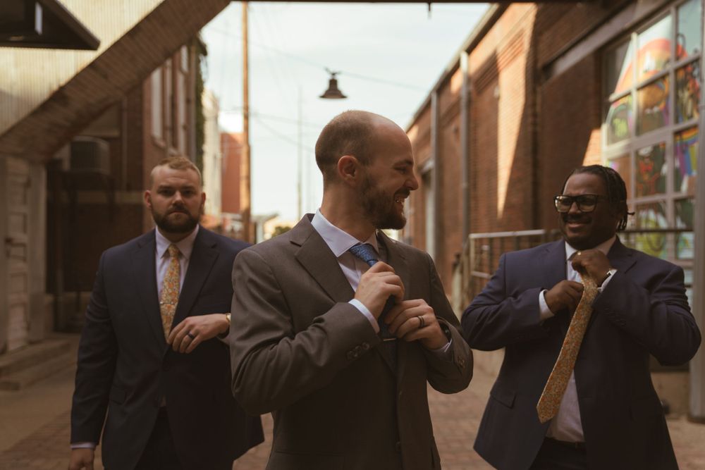 Wedding party members walking and smiling along an industrial brick building corridor.