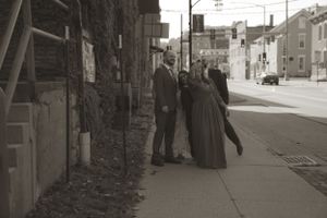 A wedding party walks down a brick-paved urban street with historic buildings in the background.