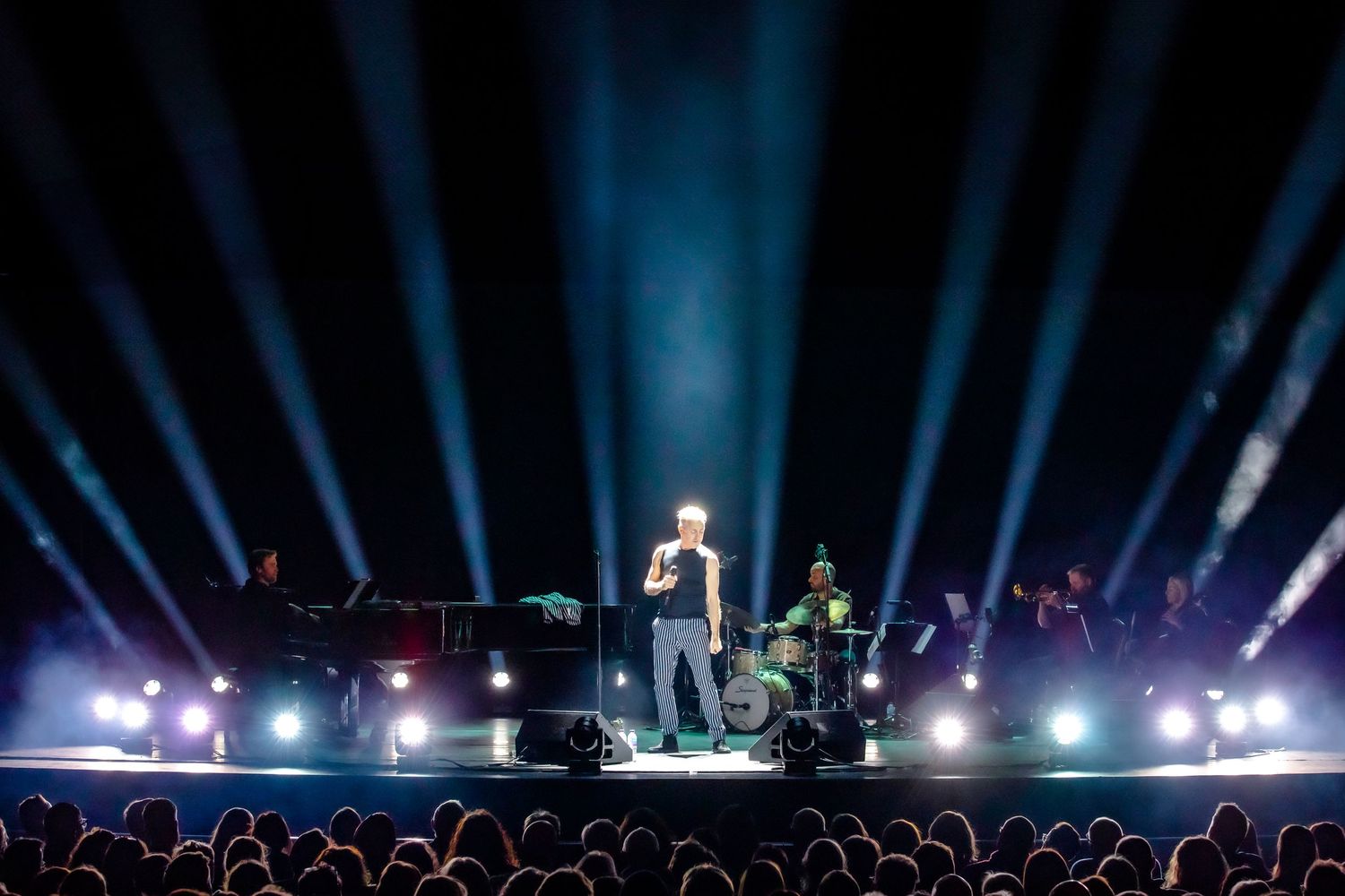 Concert stage with dramatic blue uplighting and performers silhouetted against a dark background.