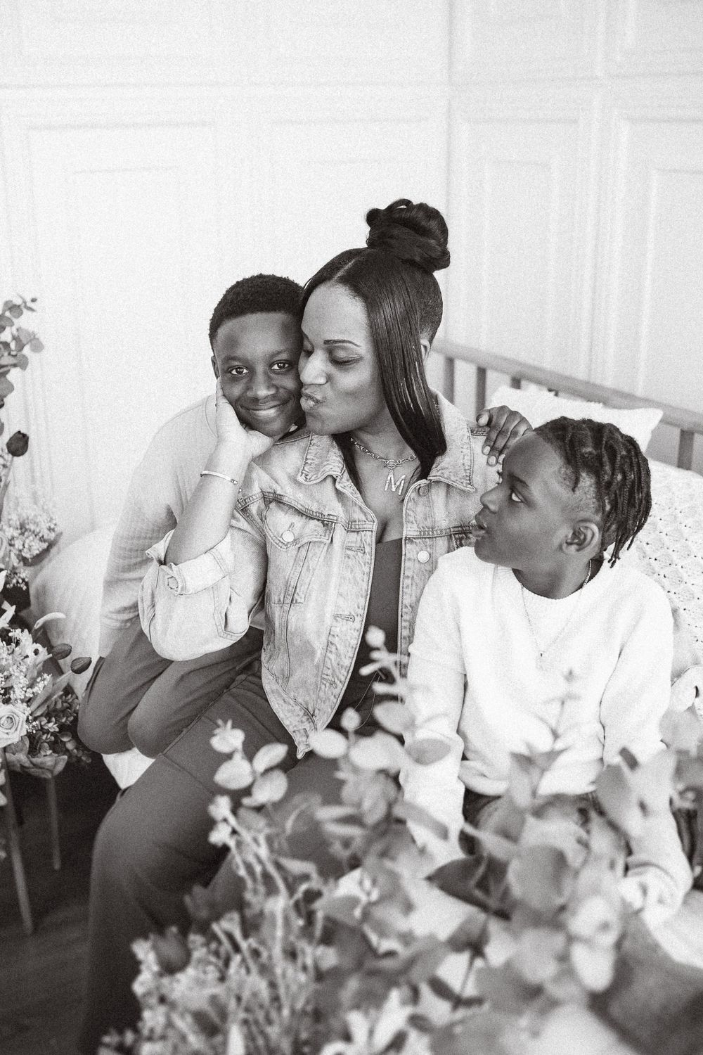 A tender black and white portrait showing a loving family moment with a mother and two children sitting together among flowers.