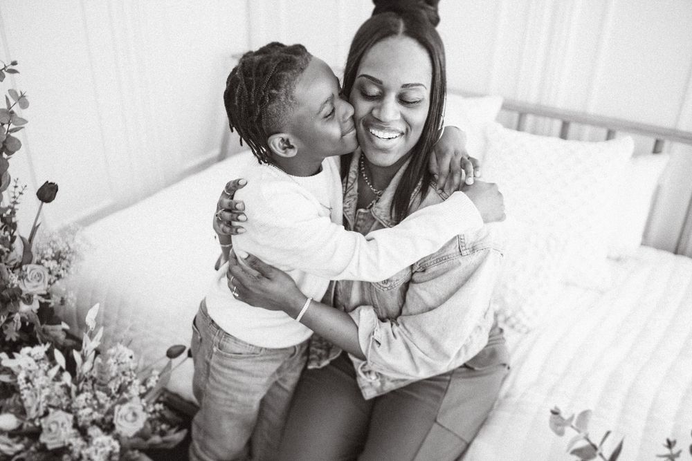 A joyful black and white moment of affection captured between parent and child on a couch with flowers nearby.
