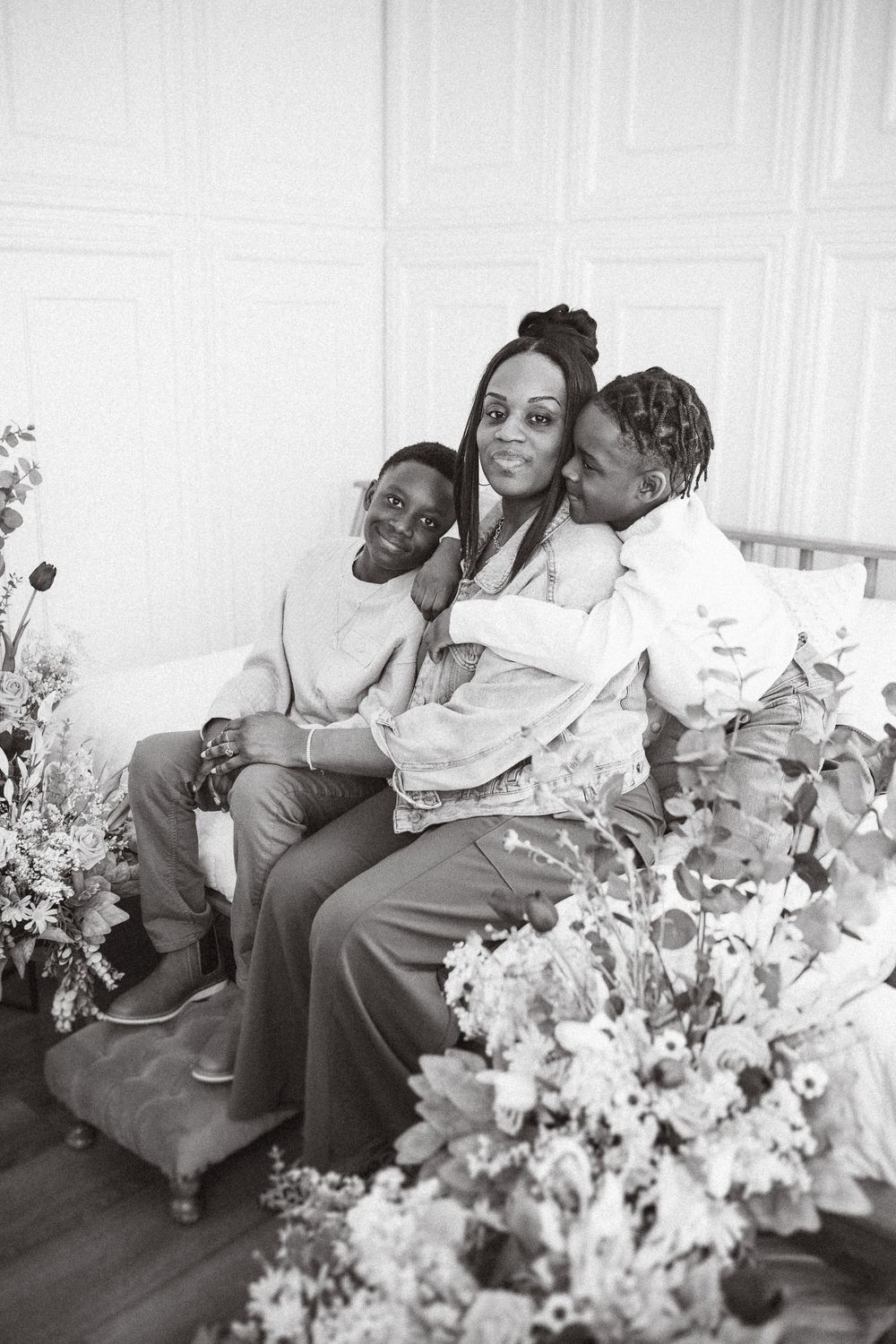 A black and white photograph showing a family sitting together on a couch with floral decorations in the foreground.