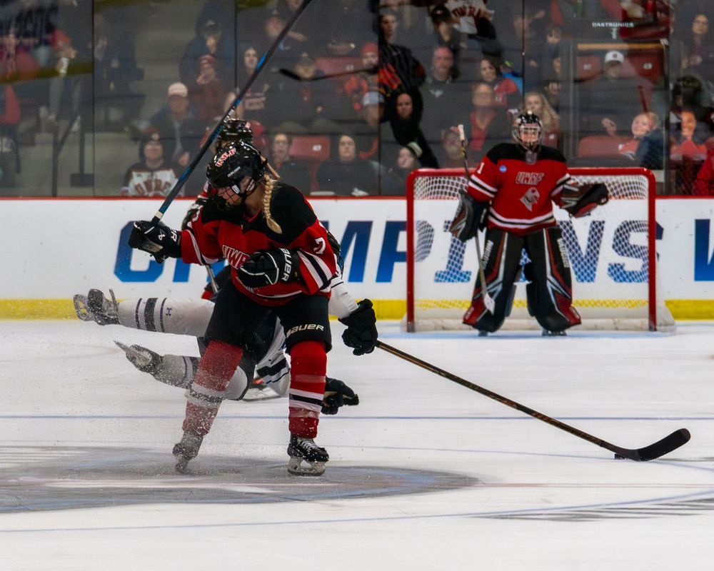 Ice hockey player in red jersey takes a shot on goal during a game while goalie defends the net.