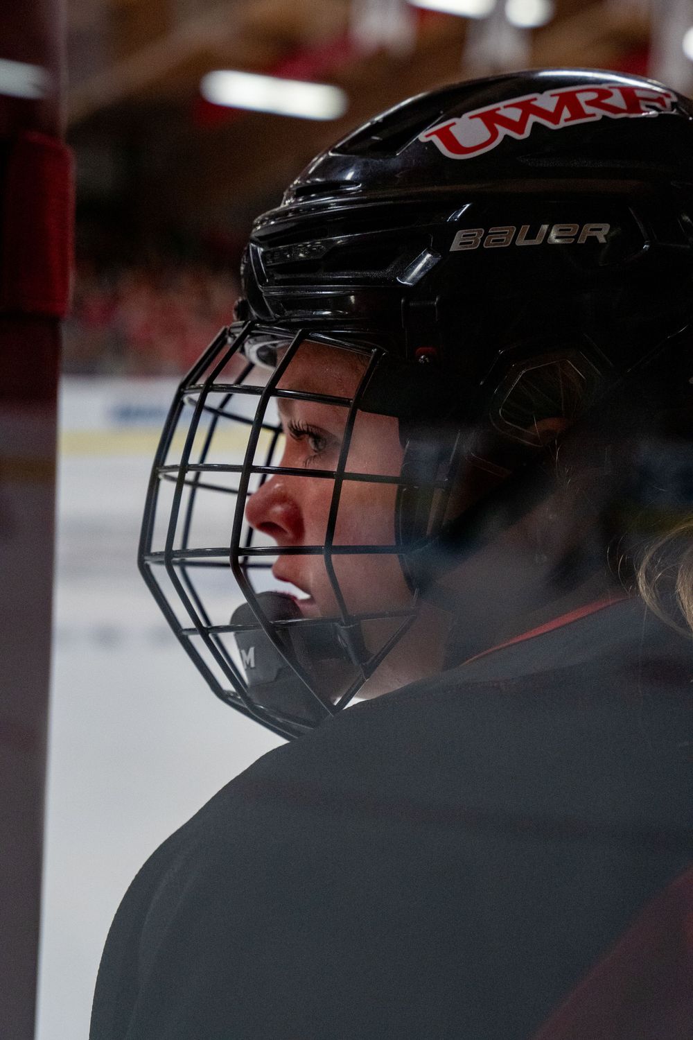 Hockey player wearing black Bauer helmet with cage and UMR logo viewed in profile during game.