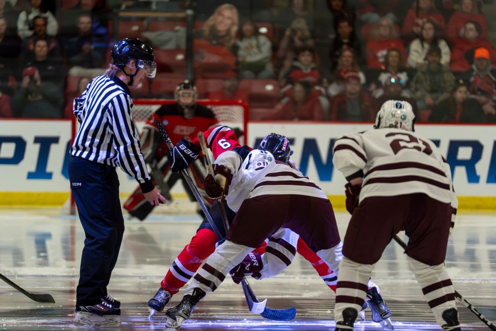Two hockey players face off at center ice while a referee watches during a competitive match.