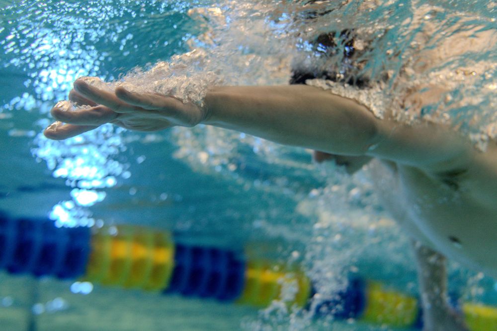 Underwater view of a swimmer doing freestyle stroke during a competitive race with lane markers visible.