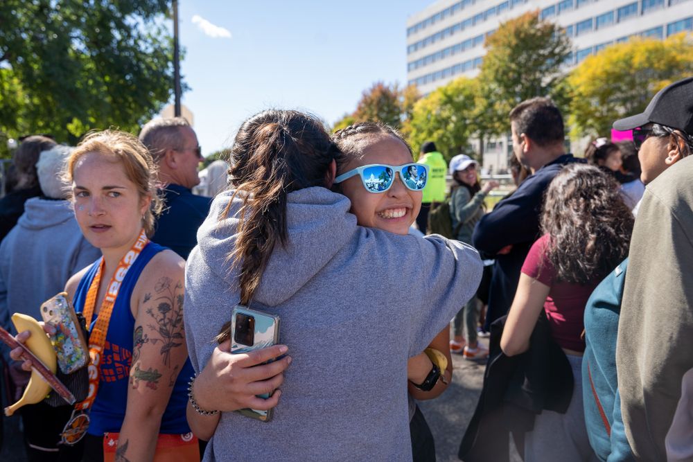 A crowd of people gather outdoors during a sunny day, holding drinks and socializing at what appears to be a public event.