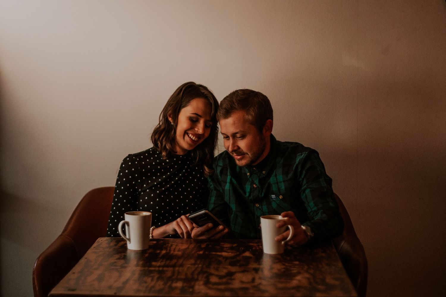A cozy indoor scene of a couple sharing coffee at a wooden table in moody lighting.