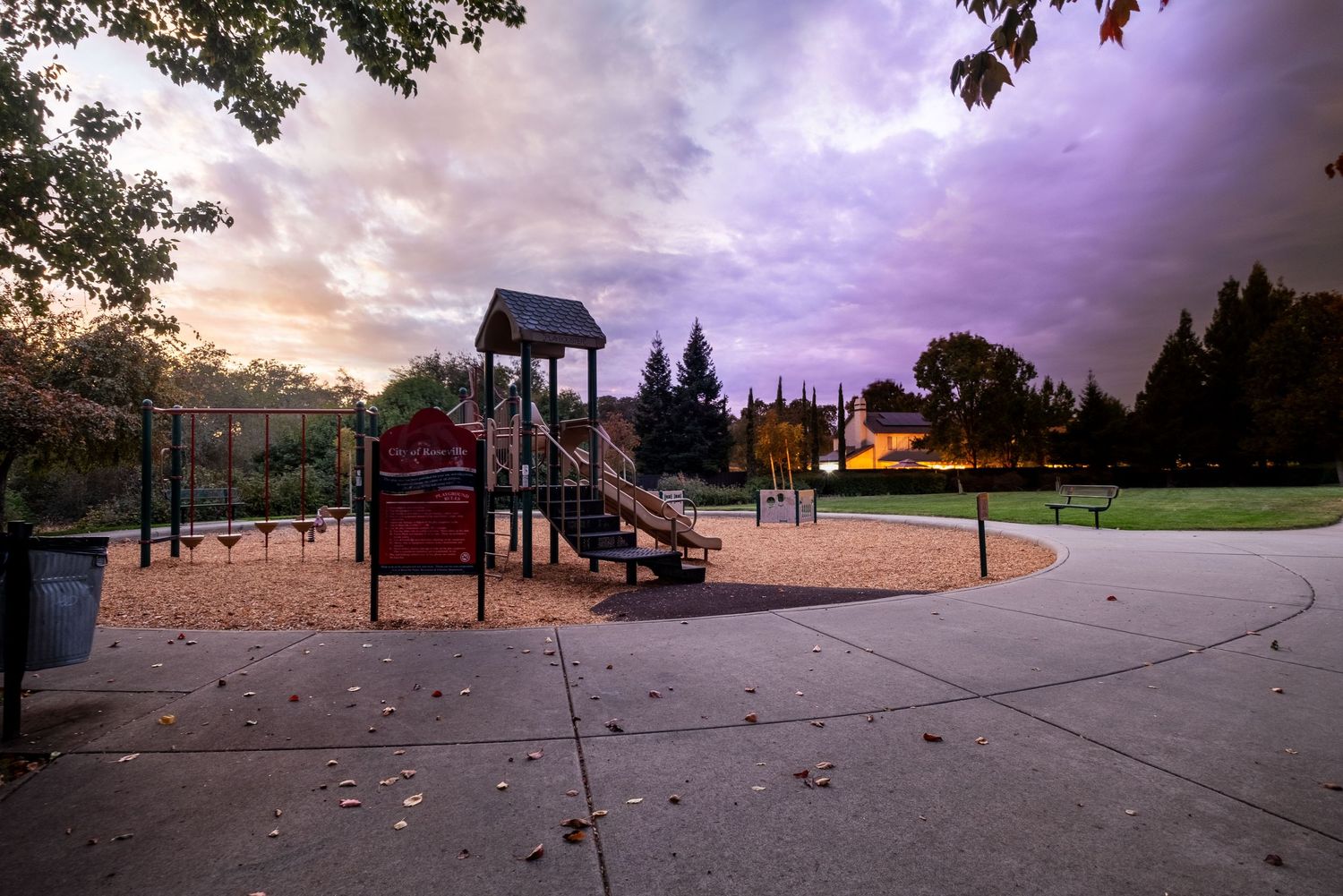 Empty playground equipment silhouetted against a dramatic purple sunset sky.