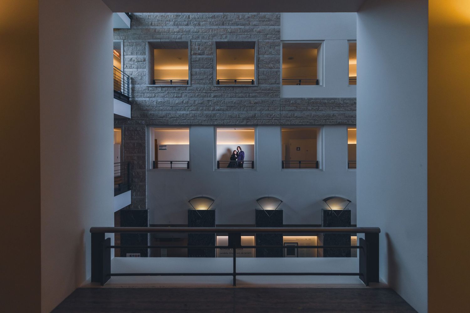 Modern architectural interior with illuminated square windows and balcony railing at dusk creates geometric patterns.
