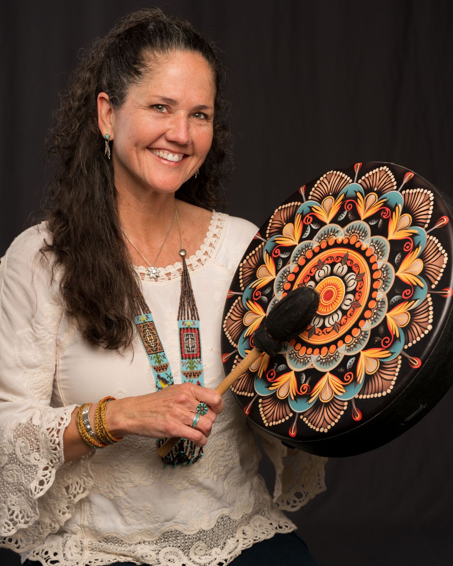 An artist displays a beautifully detailed mandala artwork painted on a round black disc with orange and turquoise patterns.