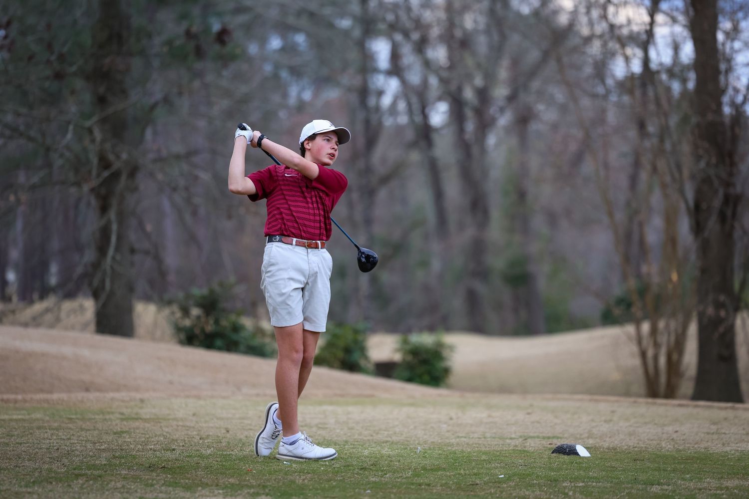 Golfer in red polo shirt takes a swing on a scenic course during golden hour.