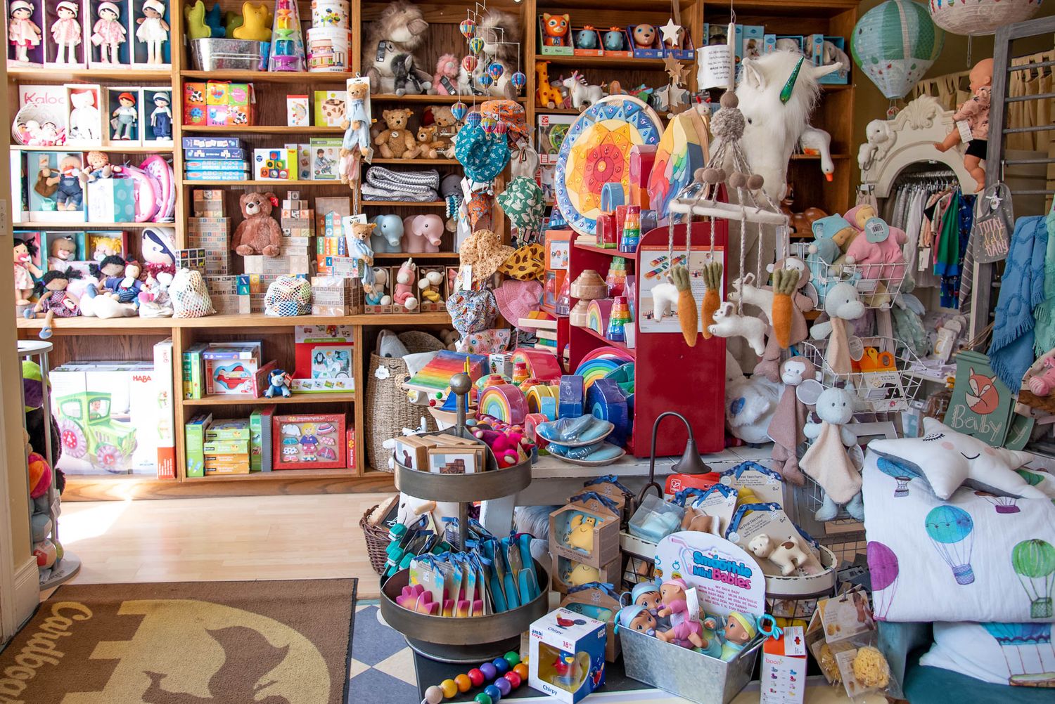 Cluttered retail shop interior displays shelves packed with toys, dolls, and various children's merchandise for sale.