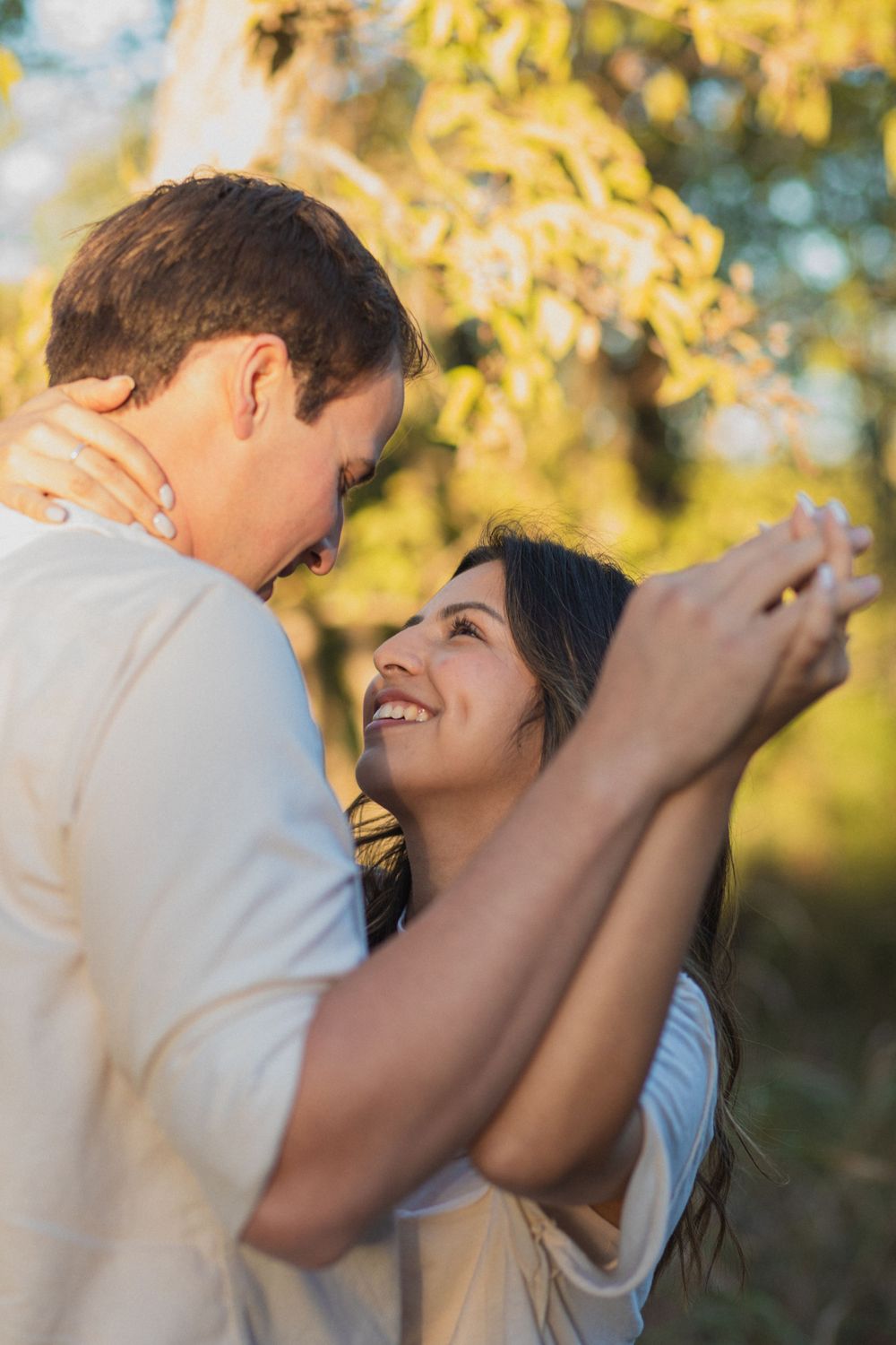 A romantic couple dancing together in warm evening sunlight with autumn trees in background.