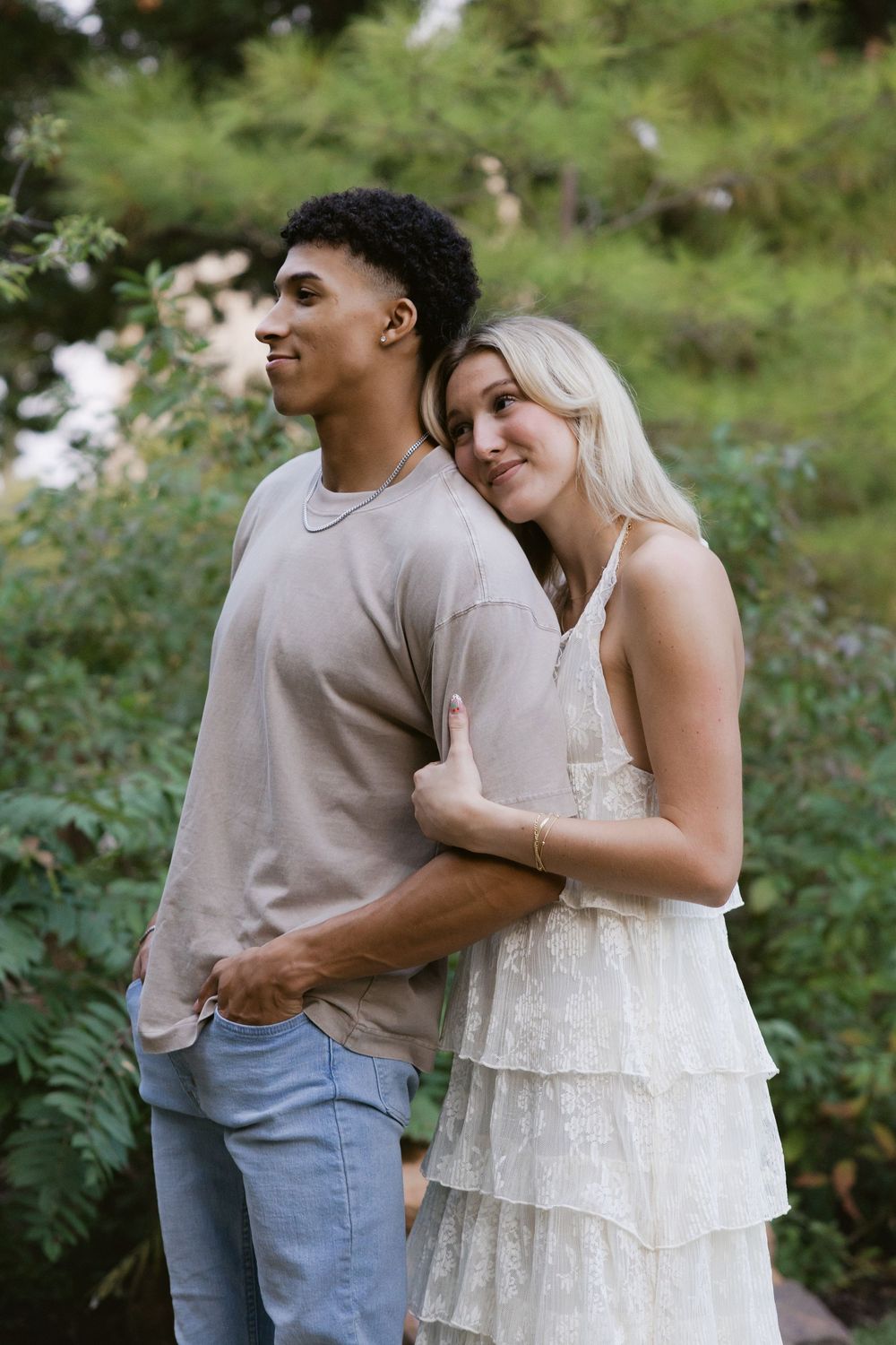 A romantic moment captured in a garden setting as a couple embraces while wearing casual and formal attire.