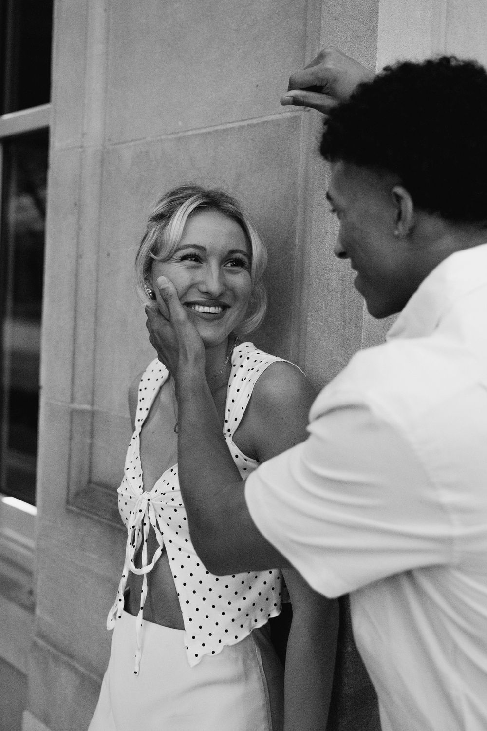 A couple laughs and shares playful moments together against a light-colored wall backdrop.
