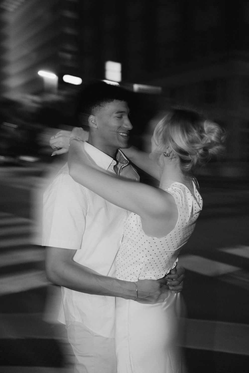 A couple dancing together in a dimly lit setting captured in black and white motion blur photography.