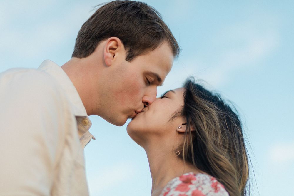 A romantic close-up moment captured against a soft blue sky background.