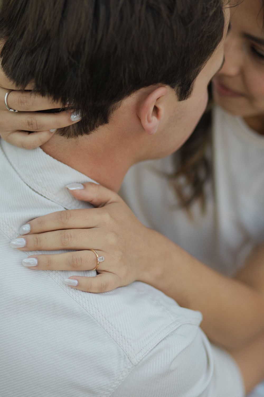 Close-up of hands with engagement ring embracing in white clothing.