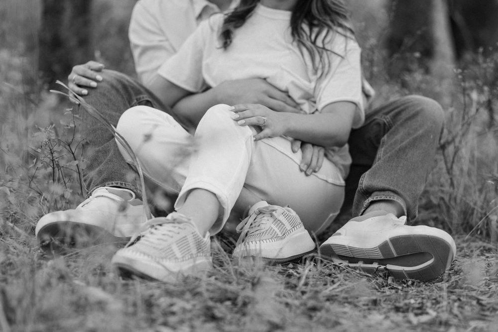 An intimate black and white photograph of a couple relaxing in a field of grass.