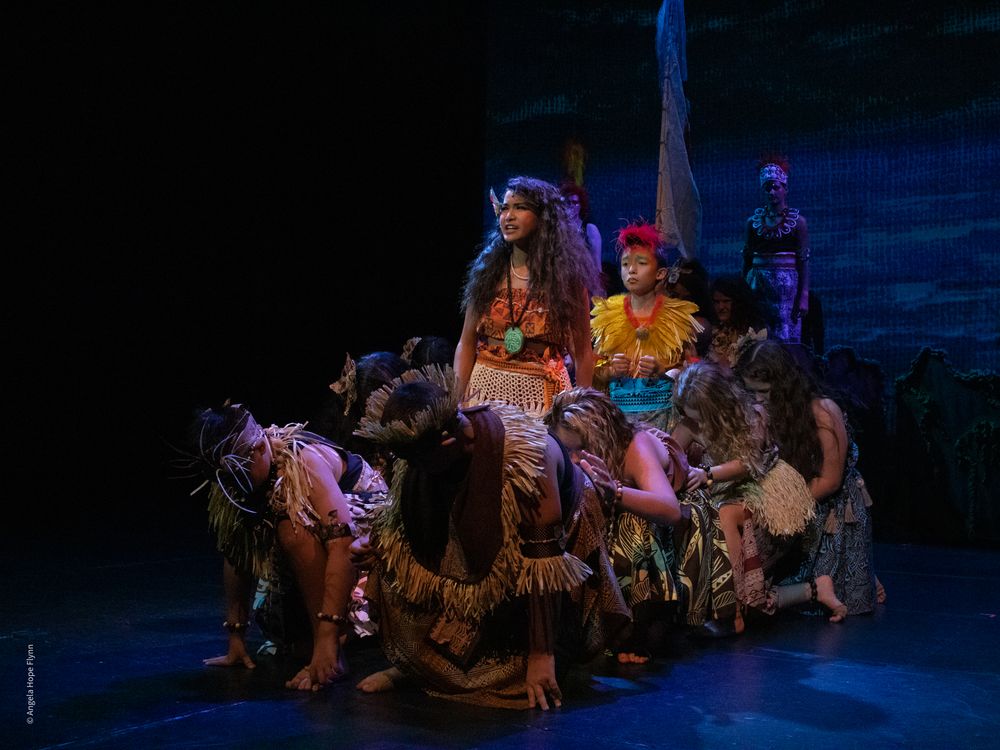 A theatrical scene with performers in fantasy costumes under dramatic stage lighting.