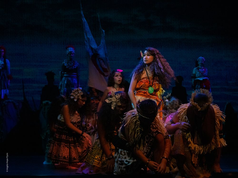 Theatrical performers in colorful costumes dance on stage during a vibrant musical production.