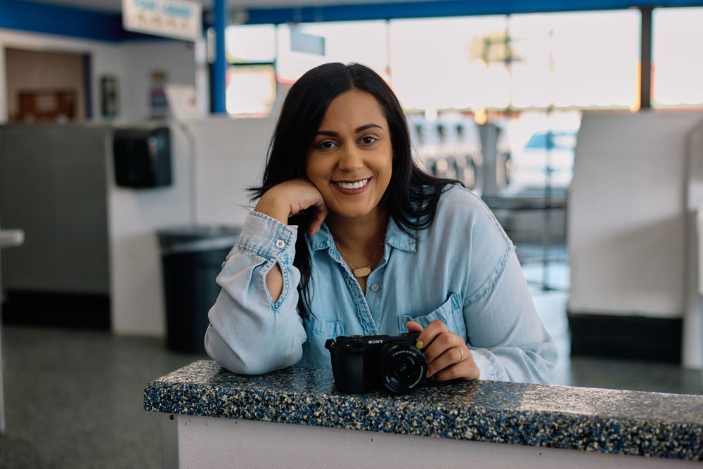 A photographer in a light blue shirt sits at a counter while holding a digital camera.