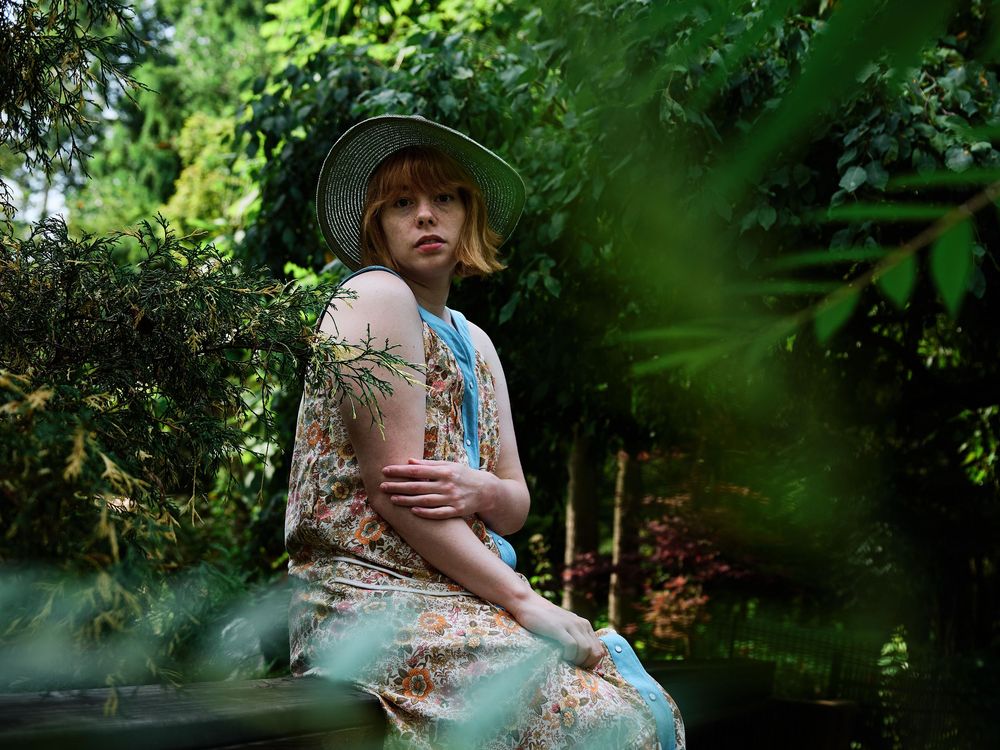 A dreamy outdoor photoshoot in lush greenery with a person in a floral dress and straw hat creating romantic portraits.