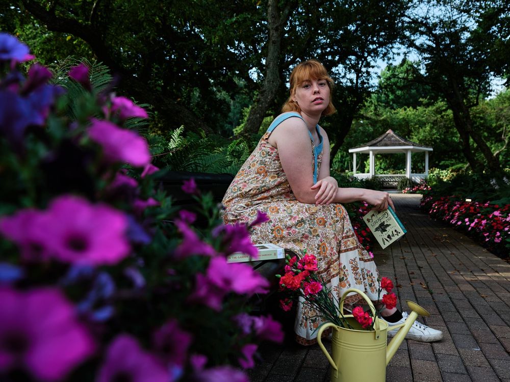 A person in a floral dress sits on a garden path surrounded by vibrant purple flowers and greenery.