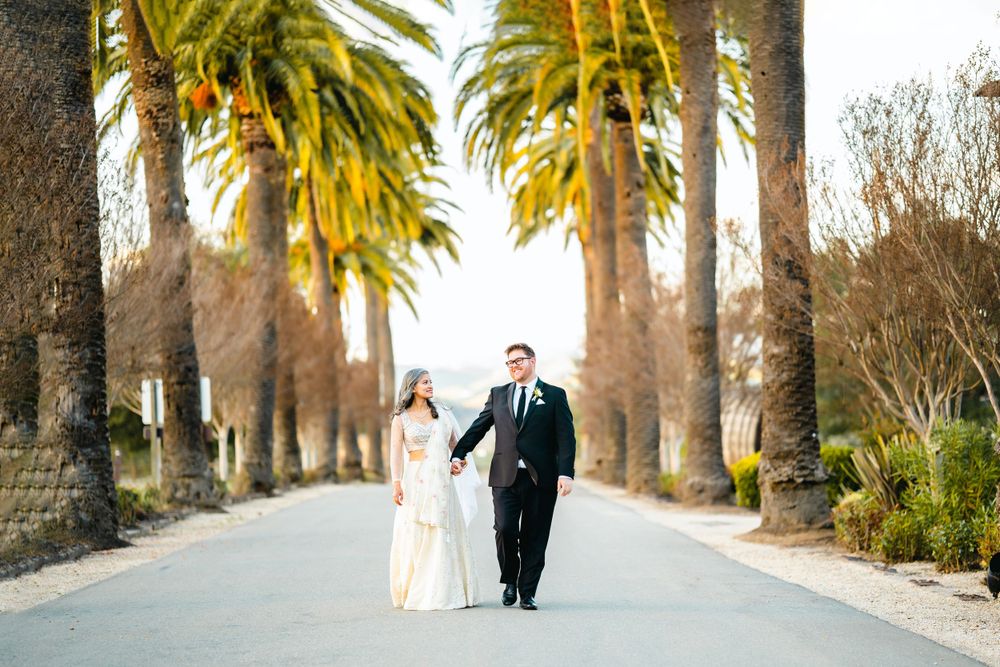 Elegant couple walks down palm tree-lined pathway in wedding attire.