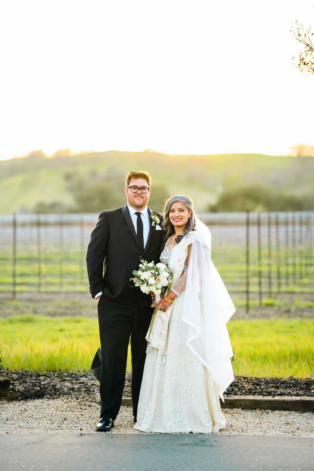 Wedding portrait at sunset with vineyard and rolling hills in background.