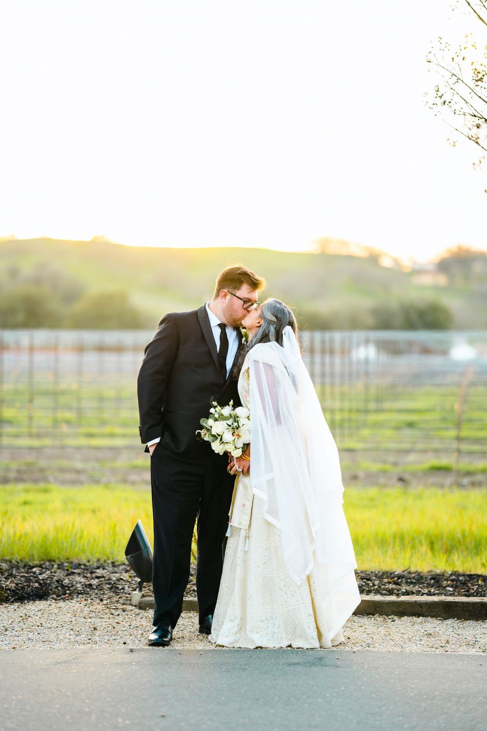 A romantic sunset wedding portrait of newlyweds sharing a tender moment in a scenic vineyard setting.