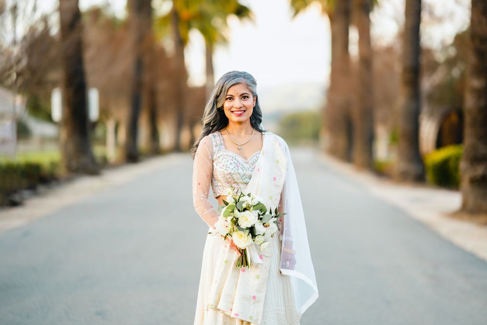 A bride in a white wedding dress poses with her bouquet on a palm tree-lined road at golden hour.